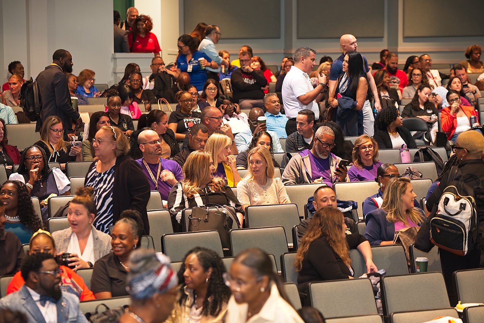 Attendees seated and talking in the auditorium ahead of a general session