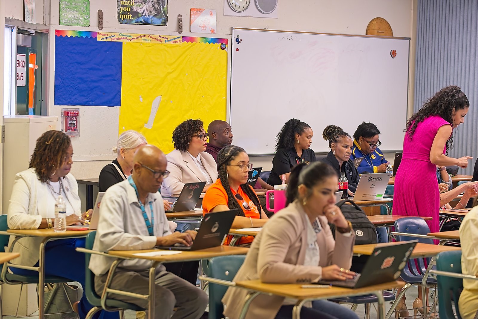 Attendees at laptops during a breakout session, colorful classroom bulletin boards behind them